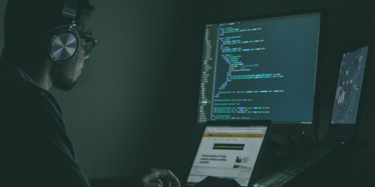 Hacker vor mehreren Bildschirmen auf denen man unter anderem Programmiercode erkennen kann